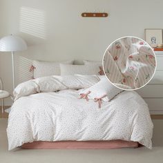 a bed with white sheets and pink flowers on it, next to a wall lamp