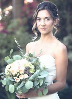 a woman holding a bouquet of flowers and greenery in her hands while looking at the camera