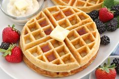 two waffles on a white plate with berries and butter sitting next to them