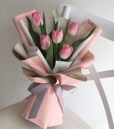 a bouquet of pink tulips tied to a white chair with ribbon on it