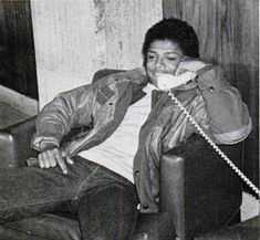 a black and white photo of a man sitting in a chair talking on the phone