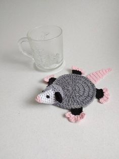 a crocheted animal sitting next to a cup