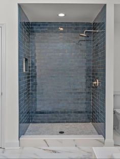 a walk in shower with blue tile on the walls and floor next to a toilet