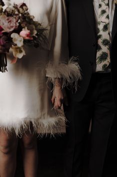 a man and woman standing next to each other in formal wear with feathers on their arms