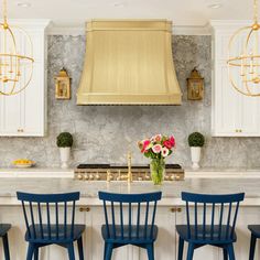 a kitchen with blue chairs and gold range hood above the stove, surrounded by marble countertops