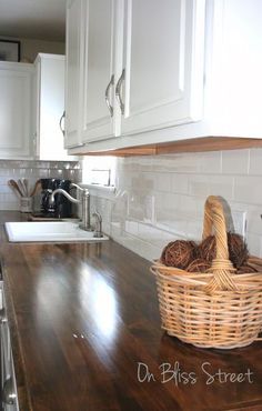 a kitchen with white cabinets and wooden counter tops, along with a basket full of clutter