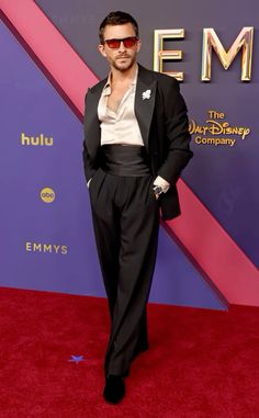 a man in a black suit and sunglasses on the red carpet at an event with his hands in his pockets