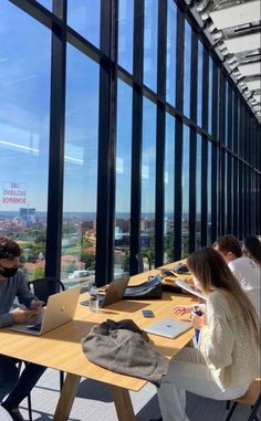 people are sitting at tables with laptops in front of large windows looking out on the city