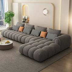 a modern living room with grey couches and orange pillows on the floor, in front of a large window