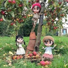 two dolls are sitting in the grass next to an apple tree with apples on it