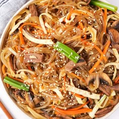 a bowl filled with noodles and vegetables next to chopsticks on a white table