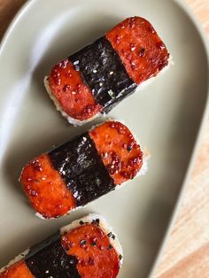 three pieces of sushi sitting on top of a white plate with black sesame seeds