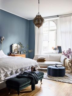 a bedroom with blue walls and white furniture in the corner, along with a large window