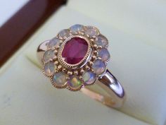 This gorgeous Ruby & Opal Vintage Inspired Flower Ring has been crafted from 9ct Solid Rose Gold. A bezel set oval cut NATURAL Ruby with surrounding NATURAL Opals brings this ring to life. Notice the stamens that surround the petals of this beautiful ring. This is an elegant Victorian inspired ring which simply looks beautiful on a lady who enjoys wearing fine jewellery from a Vintage era. THIS VINTAGE INSPIRED RUBY & OPAL RING IS TRULY AN EXQUISITE FINE JEWELLERY PIECE WHICH IS TO BE TR Victorian Rose Gold Ruby Ring, Victorian Style Cabochon Ruby Ring Gift, Victorian Style Cabochon Opal Ring Gift, Luxury Victorian Cabochon Ruby Ring, Luxury Victorian Ruby Cabochon Ring, Victorian Multi-stone Ruby Ring Gift, Opal Ring Vintage, Victorian Rings, Natural Opal