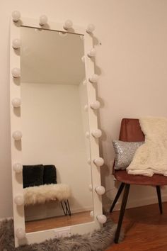 a white mirror sitting on top of a wooden floor next to a chair and pillow