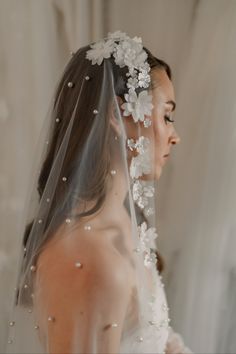 a woman wearing a veil with flowers and pearls on the head is looking down at her wedding dress