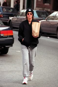 a woman walking down the street with a paper bag in her hand and cars behind her