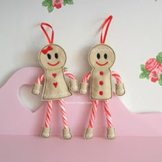 two gingerbread man and woman ornament hanging on wall next to pink background