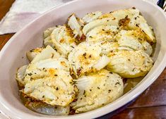 a white bowl filled with cooked artichokes on top of a wooden table