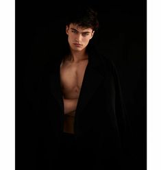 a shirtless young man is posing for a photo in the dark with his coat over his shoulders