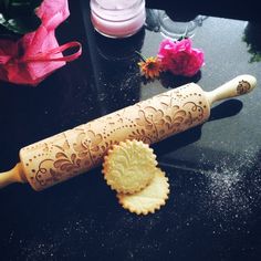 a wooden rolling pin next to some flowers on a black table with pink roses in the background