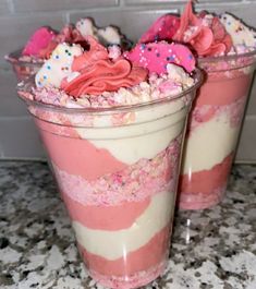 two dessert cups with pink frosting and sprinkles on them sitting on a counter