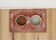 two white bowls with food in them on a red rug next to a wooden wall