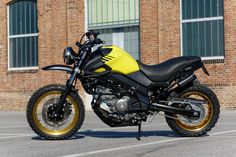 a yellow and black motorcycle is parked in front of a brick building with large windows