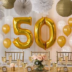 a 50th birthday party with gold balloons and white paper flowers on the table in front of it