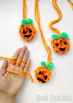 a hand holding an orange string with two pumpkins attached to it and another piece of yarn