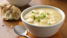 a white bowl filled with soup next to a piece of bread on top of a wooden table