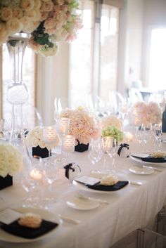 the table is set with white flowers and black napkins, wine glasses and candles