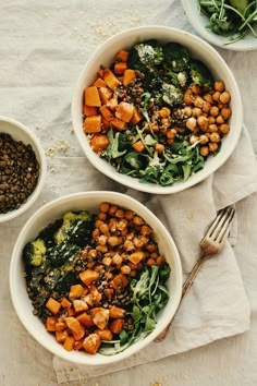 three bowls filled with different types of food on top of a white cloth next to silverware