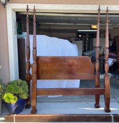 a wooden bed frame sitting on top of a sidewalk next to potted plants and an open garage door