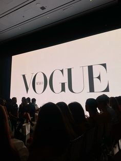 a group of people sitting in front of a large screen with the word vogue on it