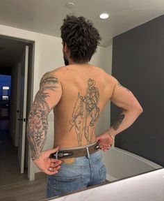 a man with tattoos on his back is looking at himself in the mirror