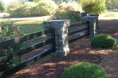 a wooden fence surrounded by bushes and flowers in a park area with pink roses on either side