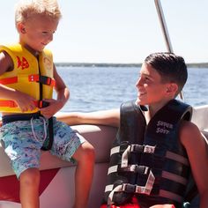 a young boy sitting on the back of a boat next to a man in life vest