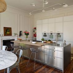 a kitchen with white cabinets and stainless steel counter tops, along with chairs around a dining room table