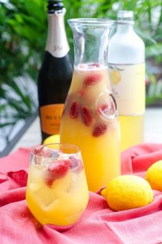 three bottles and two glasses filled with lemonade sit on a table next to some fruit