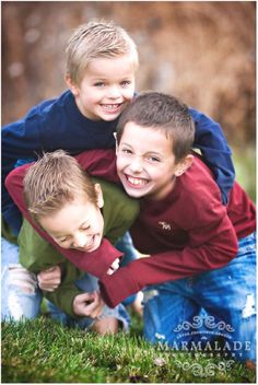 three young boys posing for a photo in the grass with their arms around each other