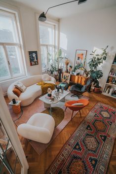 a living room filled with lots of furniture and plants on top of a hard wood floor