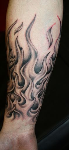 a man's arm with black and grey flames on it, as well as his hand