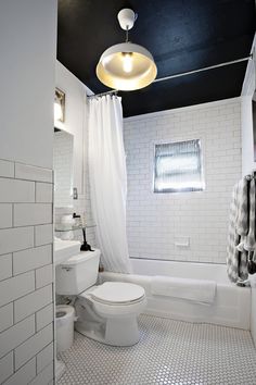 a white toilet sitting next to a bath tub under a light hanging from a ceiling