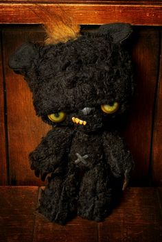 a black stuffed animal with yellow eyes sitting on top of a wooden table next to a wall