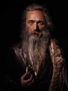 an old man with long hair and beard holding a pipe in his right hand while wearing a leather jacket