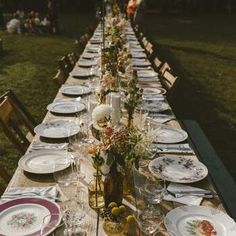 a long table is set with plates and place settings for an outdoor dinner in the grass