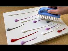 a person using a brush to clean toothbrushes on a white tray with red and blue handles