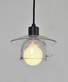 a clear glass light fixture hanging from a black wire and white wall behind it is a bulb that has been turned on