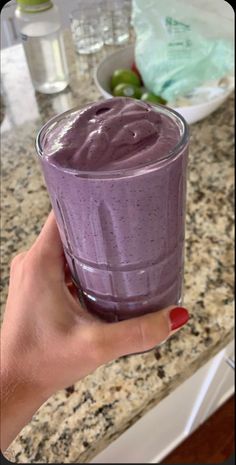 a hand holding a glass filled with purple liquid on top of a marble countertop